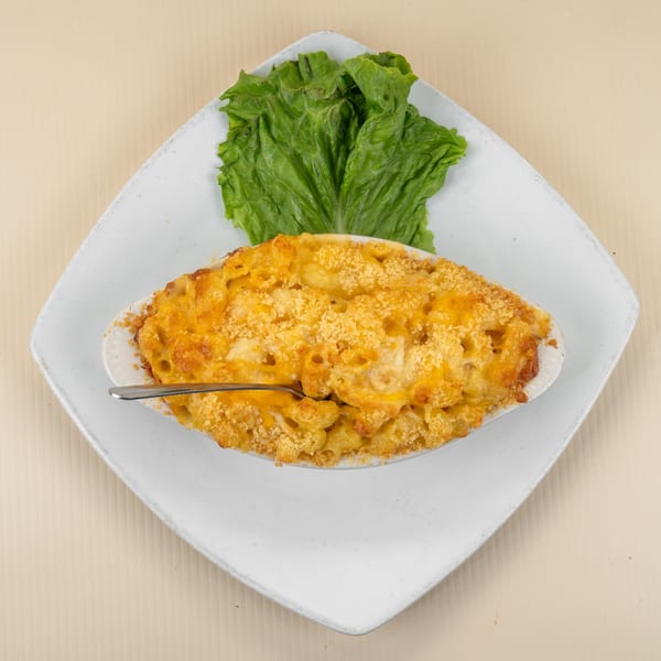 Baked macaroni and cheese in a white oval dish with a spoon, garnished with lettuce.