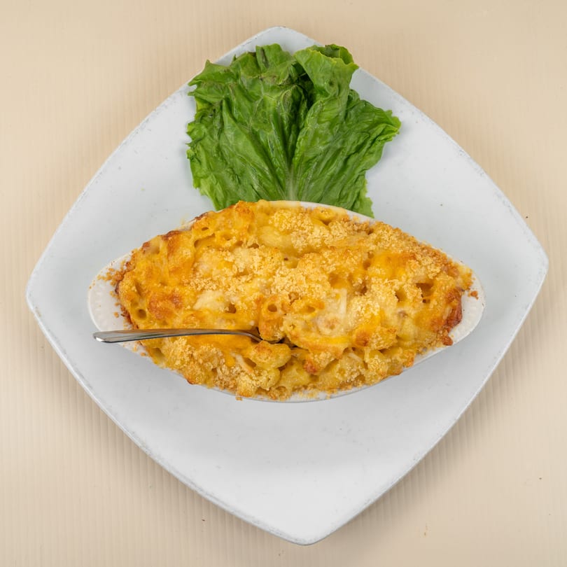 Baked macaroni and cheese in a white oval dish with a spoon, garnished with lettuce.