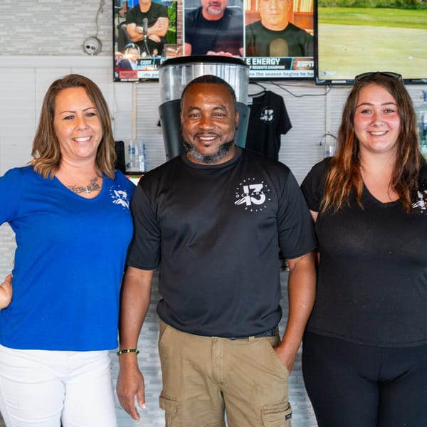 Three smiling Oceans 13 Sports Bar & Grill staff members stand together in front of TVs.