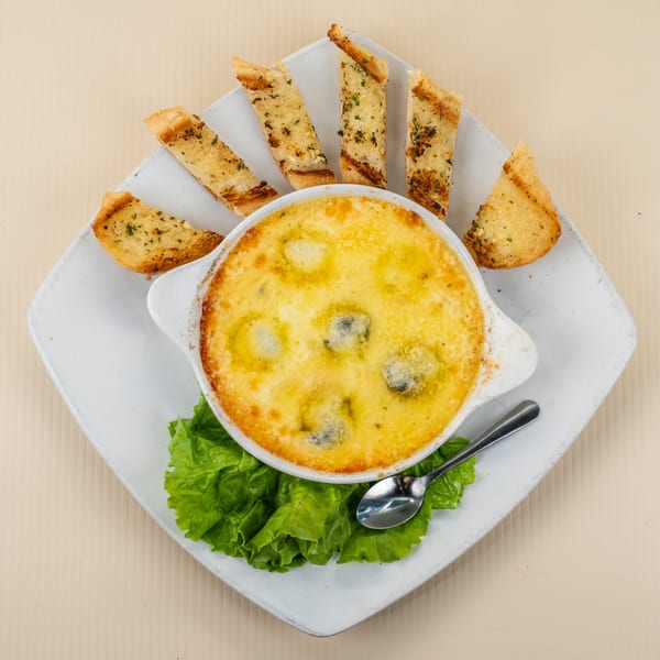 Baked escargots in a creamy sauce with garlic bread slices and lettuce on a white plate.