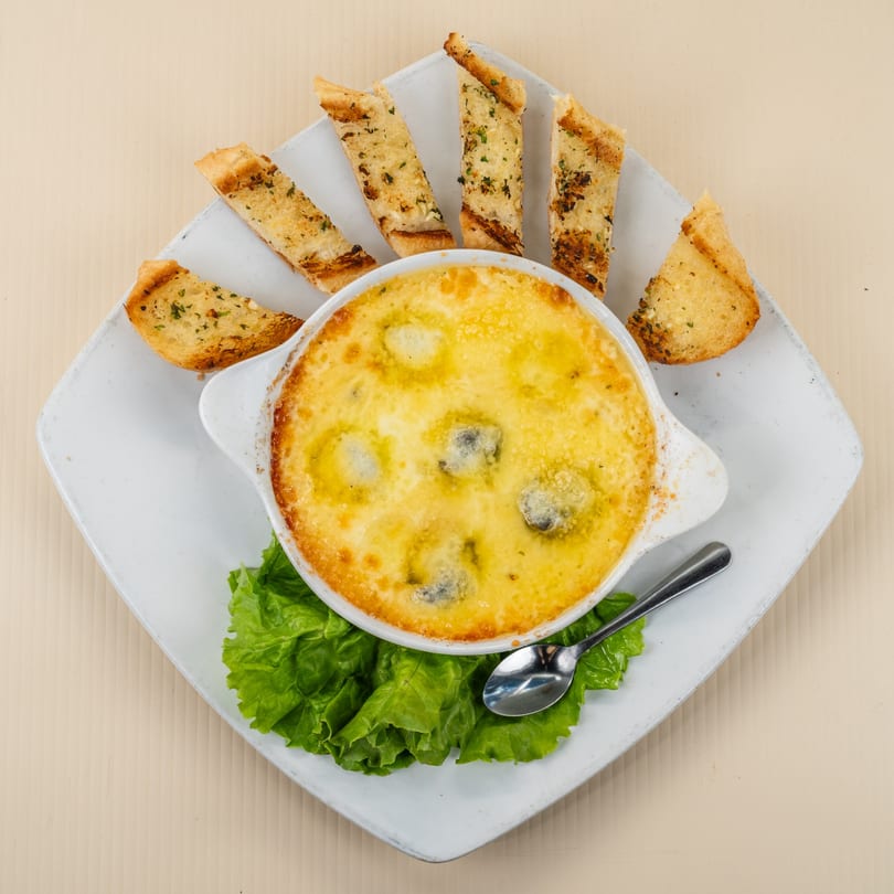 Baked escargots in a creamy sauce with garlic bread slices and lettuce on a white plate.