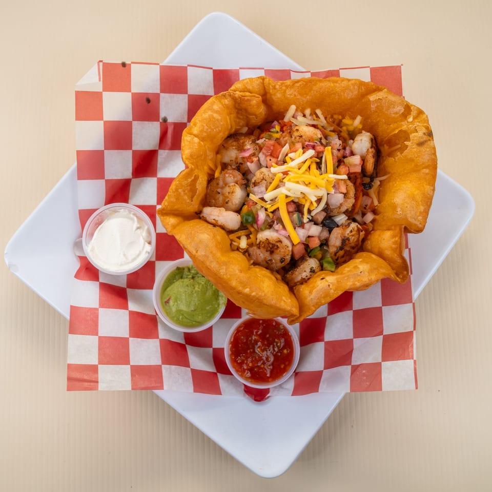 Shrimp taco salad in a crispy fried tortilla bowl with sides of sour cream, guacamole, and salsa.