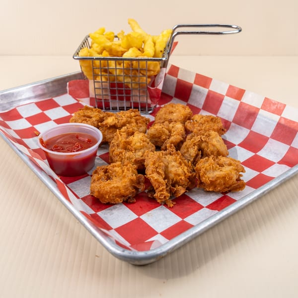 Fried chicken nuggets, a side of fries in a metal basket, and ketchup on a red checkered tray.