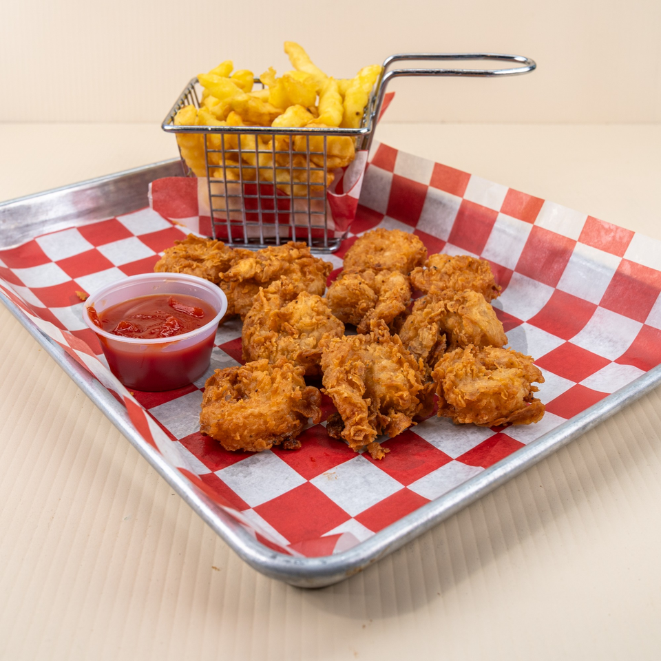 Fried chicken nuggets, a side of fries in a metal basket, and ketchup on a red checkered tray.