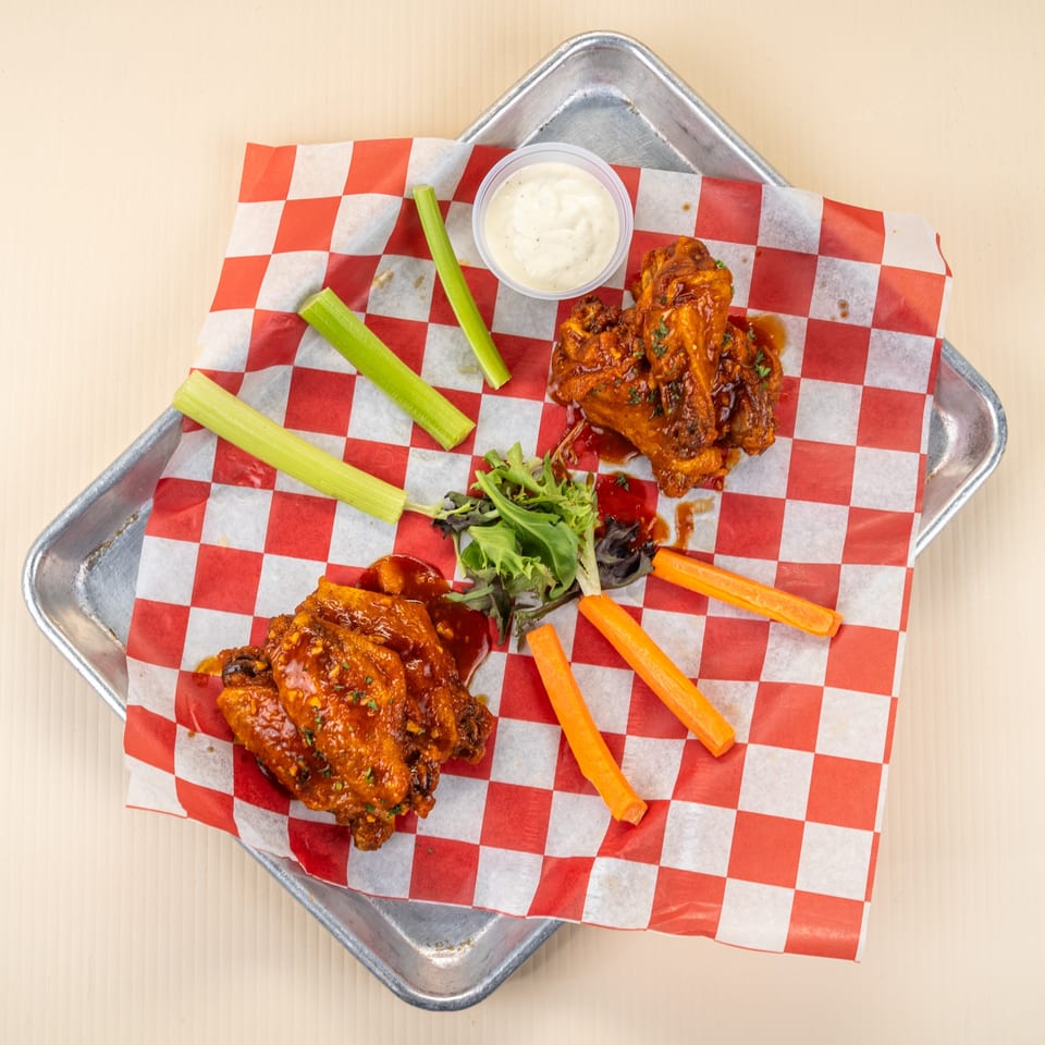 Spicy chicken wings with celery, carrots, and ranch dressing on red and white checkered paper.