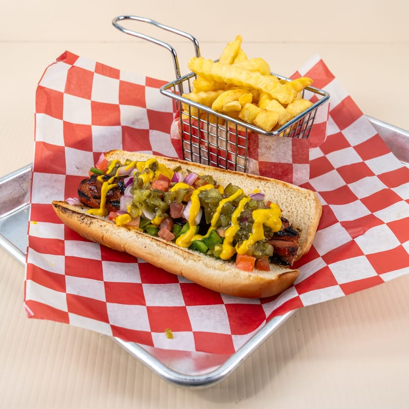 Gourmet hot dog with relish, onions, tomatoes, and mustard, served with a side of fries.