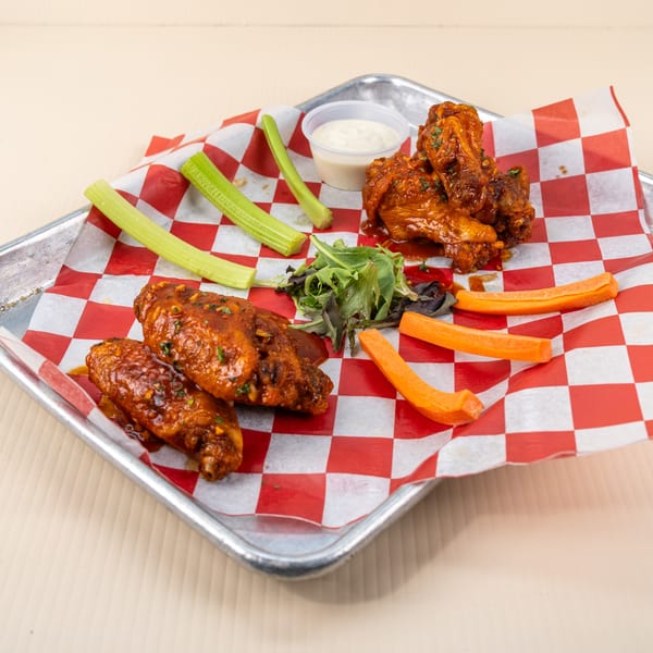 Spicy chicken wings with celery, carrots, and ranch dressing on a red and white checkered paper.