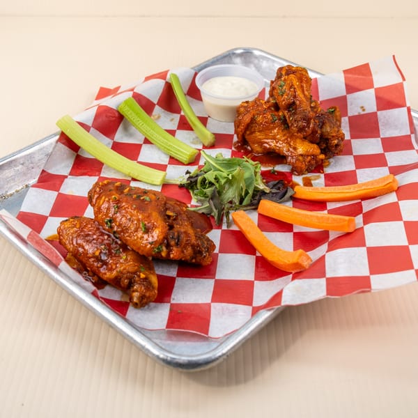 Spicy chicken wings with celery, carrots, mixed greens, and ranch dressing on a checkered paper.
