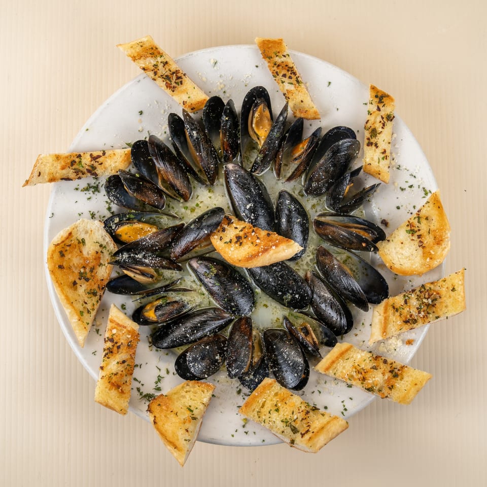 Steamed mussels in a white wine sauce with garlic bread on a white plate.