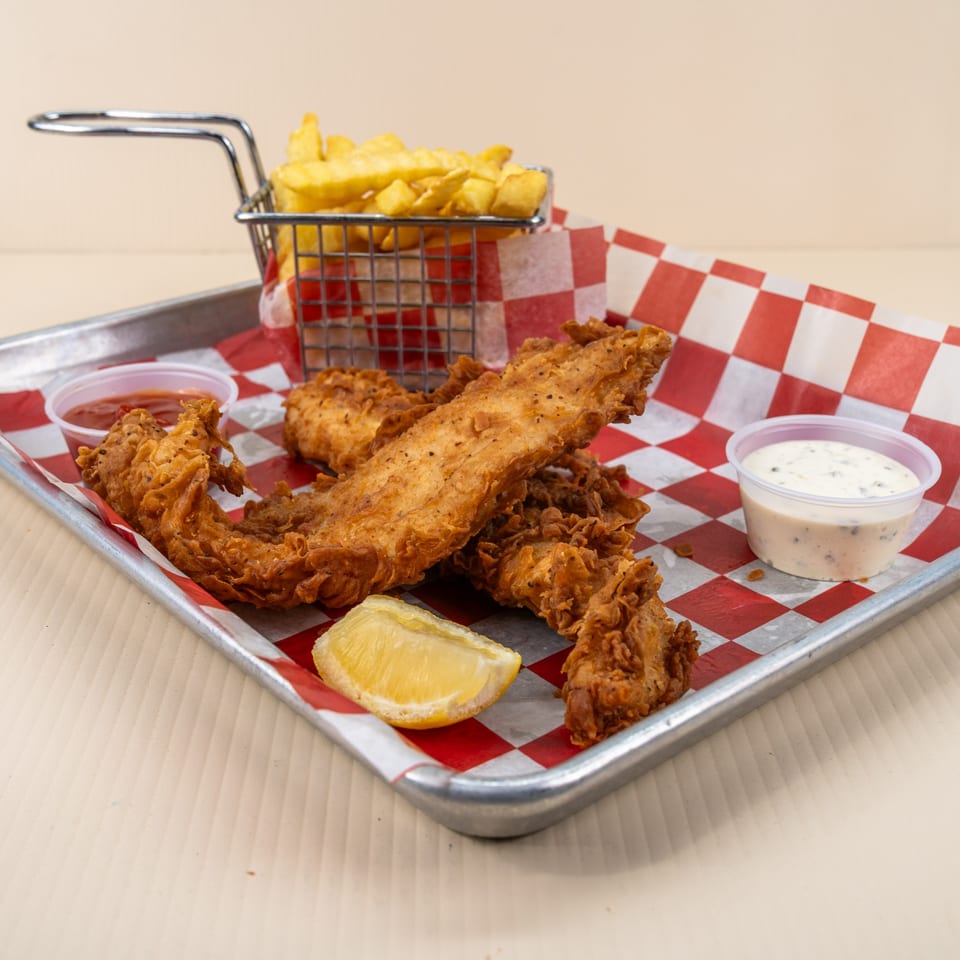 Crispy fried fish fillets with crinkle-cut fries, lemon wedge, ketchup, and tartar sauce on a tray.