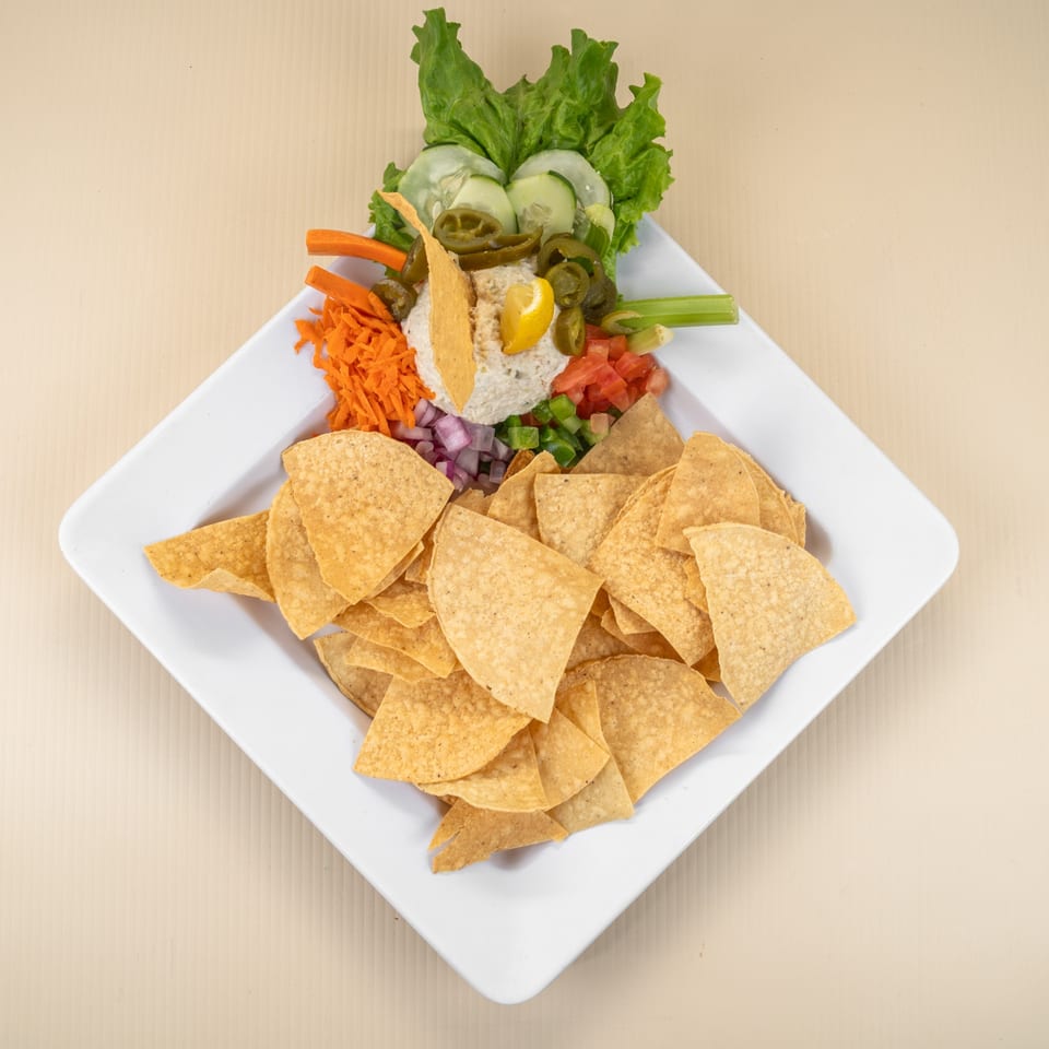 White plate with tortilla chips, a dip, and various vegetable garnishes including lettuce, carrots, and jalapenos.