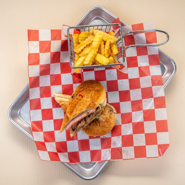 Cuban sandwich with ham, pork, and cheese, served with crinkle-cut fries in a metal basket.
