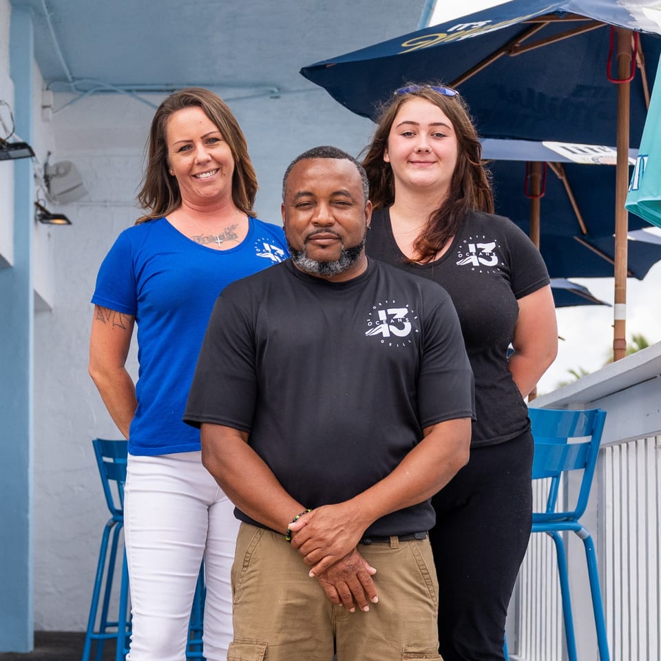 Three Oceans 43 Grill staff members, two women and one man, stand smiling on an outdoor patio.