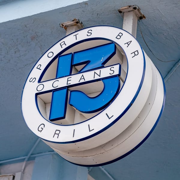 Round white and blue sign for "17 Oceans Sports Bar & Grill" hanging from a light blue ceiling.