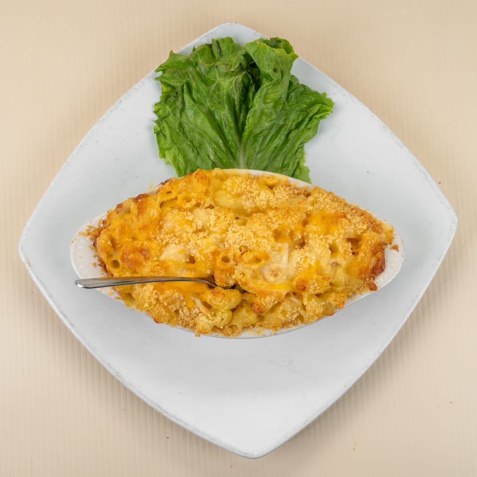 Baked mac and cheese in a white oval dish with a spoon, garnished with lettuce on a white plate.