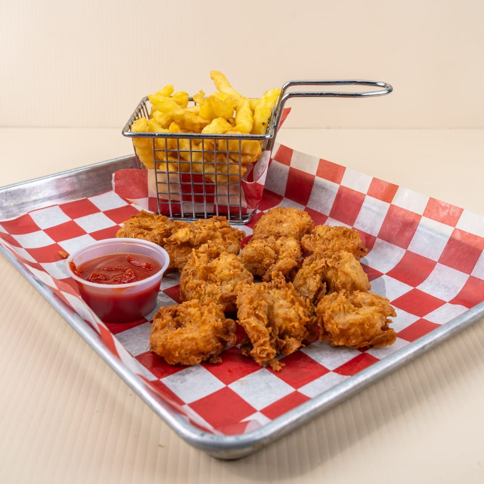Fried chicken nuggets, a side of fries in a metal basket, and ketchup on a checkered tray.