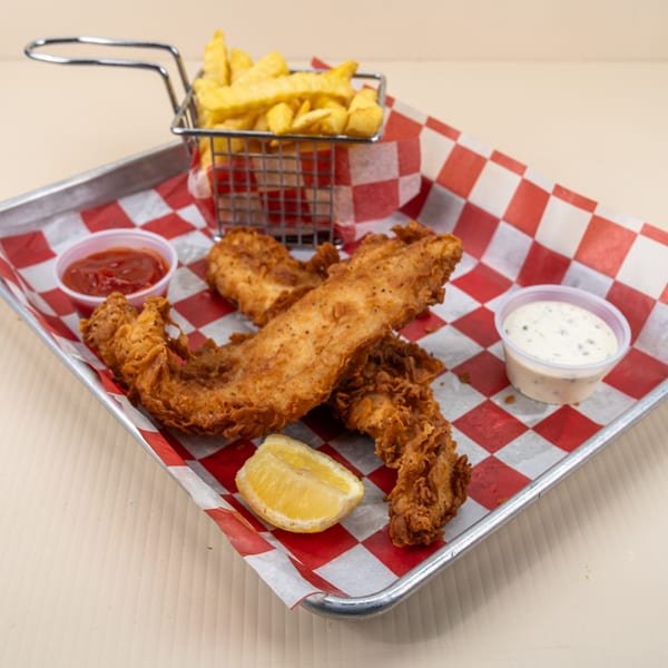 Crispy fried fish fillets, a basket of fries, ketchup, tartar sauce, and a lemon wedge on a tray.