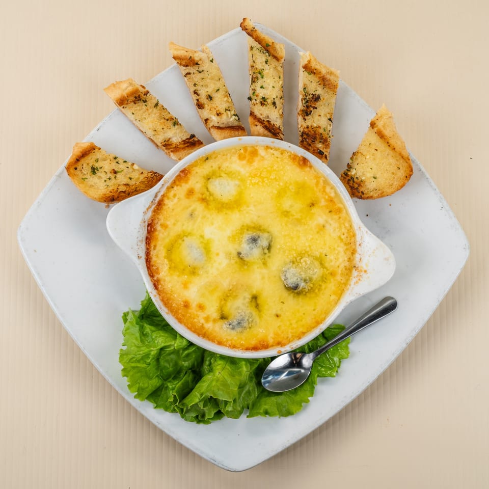 Baked escargots in a white dish with melted cheese, served with garlic bread and lettuce.