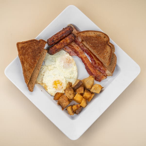 Full breakfast plate with fried eggs, bacon, sausage, toast, and home fries.