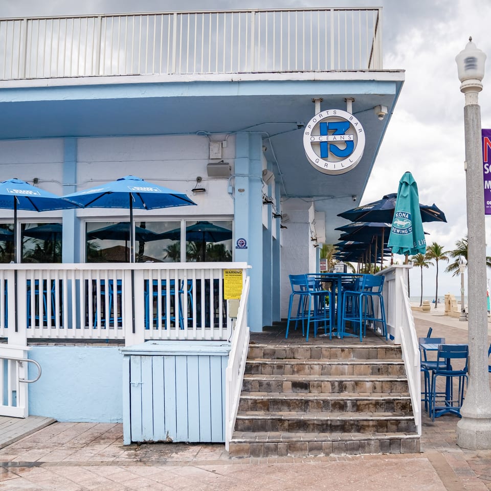Oceans 13 Sports Bar and Grill, a blue and white building with outdoor seating and umbrellas.