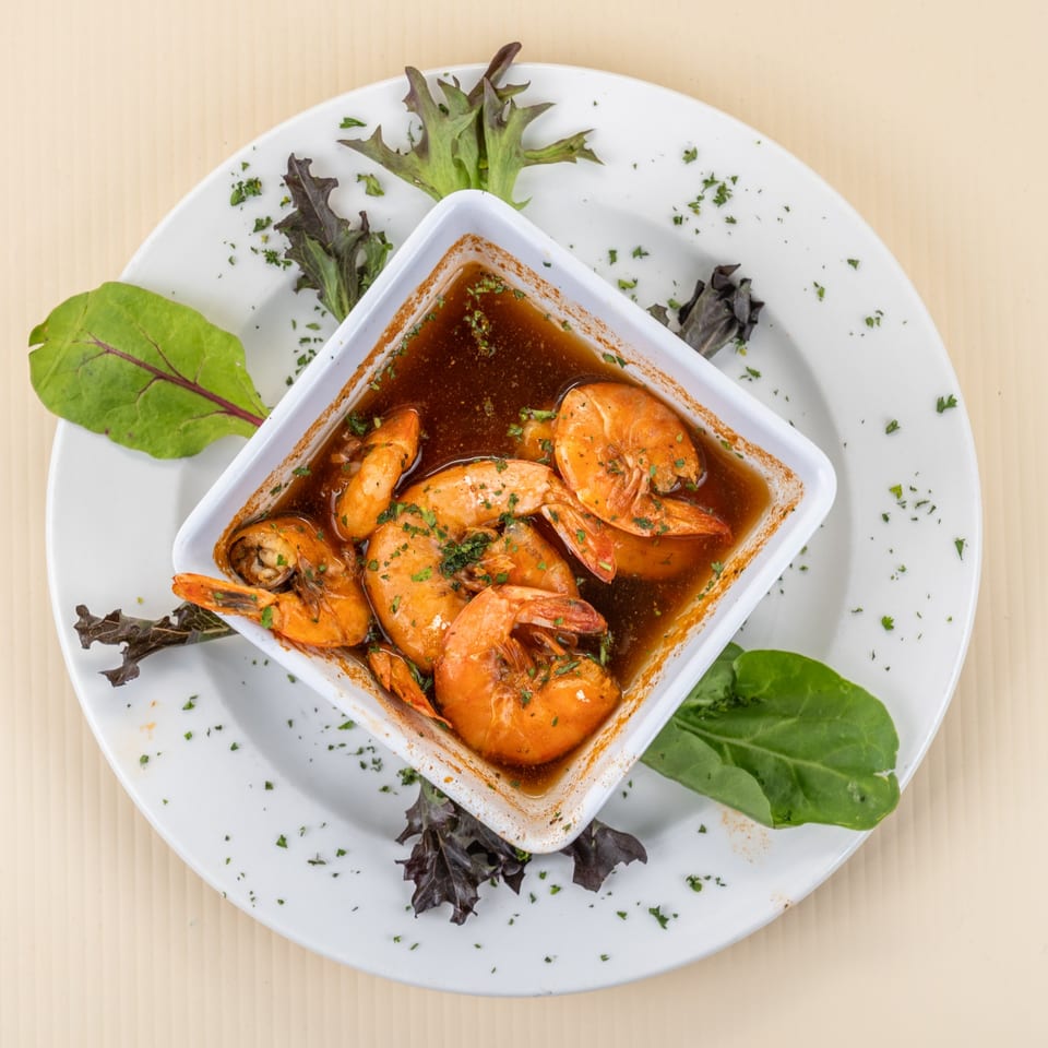 Shrimp scampi in a white square bowl with a dark sauce, garnished with parsley and lettuce.