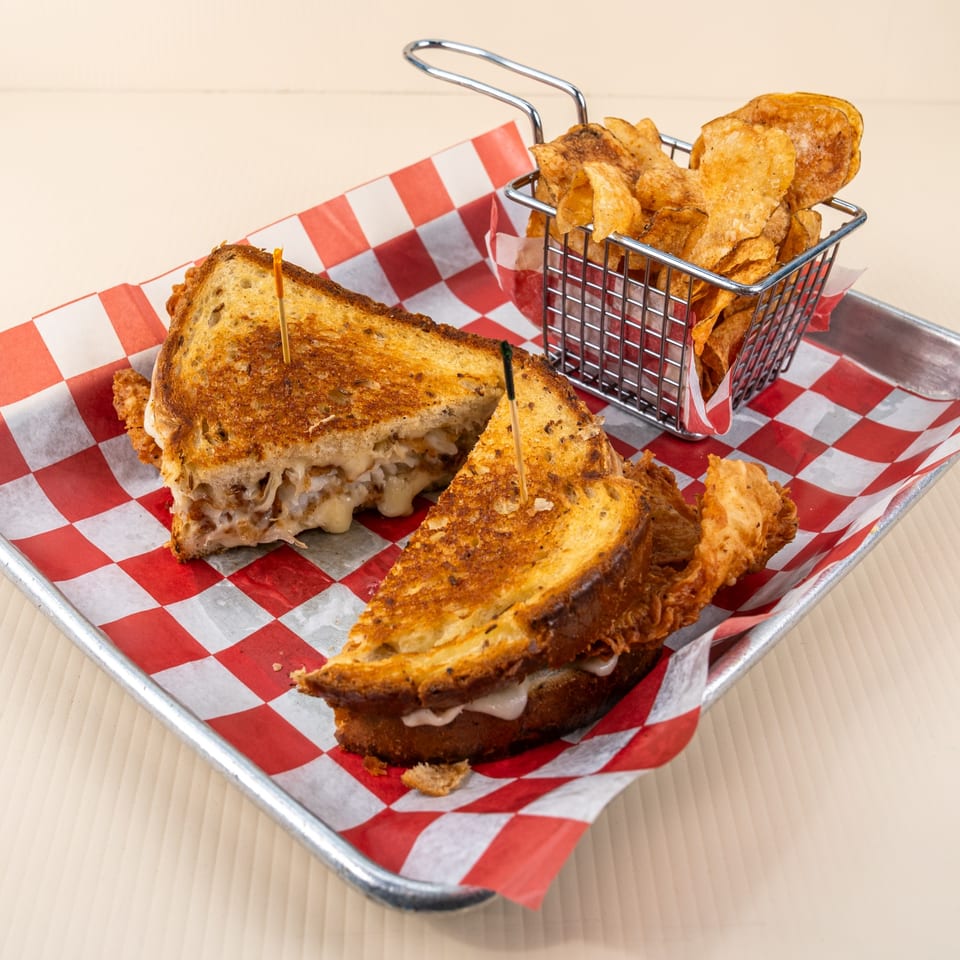 Grilled cheese sandwich cut in half, served with a side of potato chips in a metal basket.